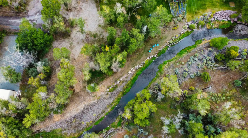 Aerial view of a winding creek surrounded by lush greenery and rocky banks, with kayaks lined up along the shore.